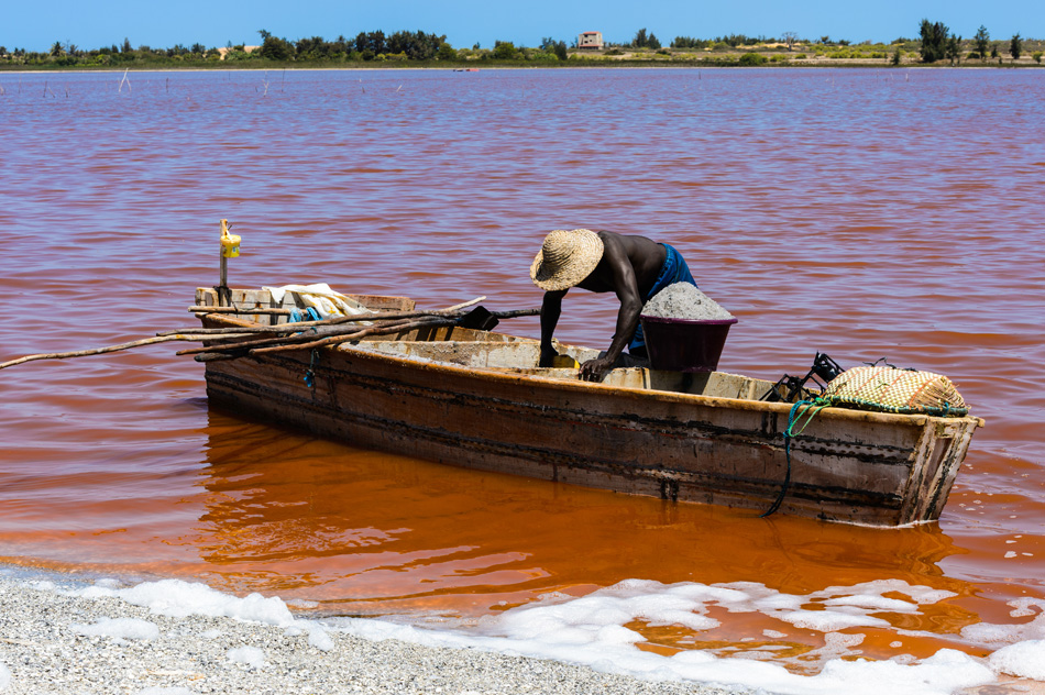 African man on the wooden boat over the Senegal red lake, called Lake Retba or Lac Rose